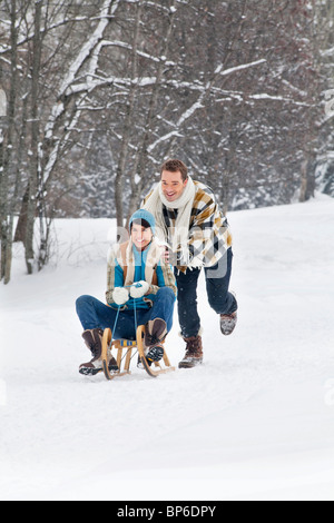 Young man pushing woman on sled Stock Photo