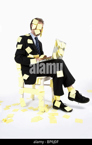 A man covered in blank adhesive notes while sitting and using a laptop Stock Photo