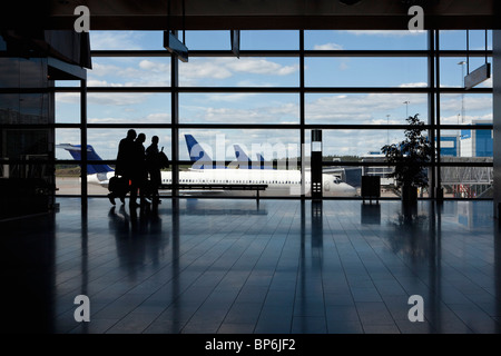 Three business people walking by a window of an airport, silhouette Stock Photo