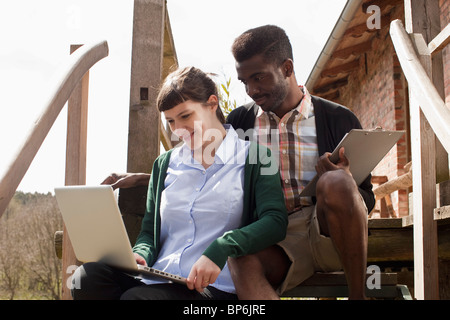 A couple sitting on a staircase, looking at a laptop together Stock Photo