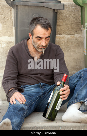 poor drunk man lying near trashcan in city street Stock Photo