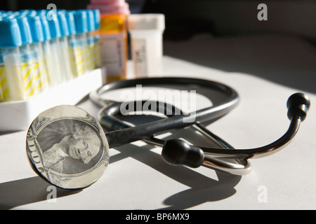 A stethoscope with a dollar bill on it and medicine in the background Stock Photo