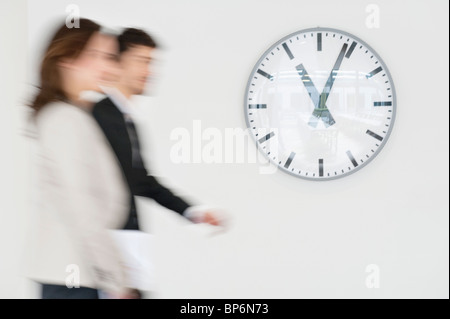 Business executives walking together in front of a wall clock Stock Photo