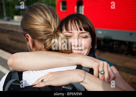 An happy woman hugs her boyfriend on a train platform Stock Photo