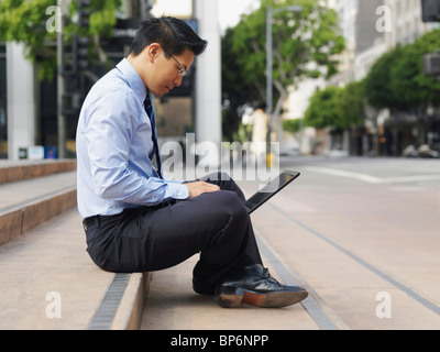 A businessman sitting cross-legged on some steps, using a laptop Stock Photo