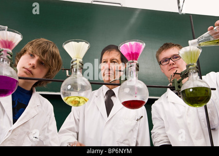 A teacher supervising two students conducting a chemistry experiment Stock Photo