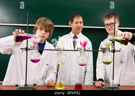 A teacher supervising two students conducting a chemistry experiment Stock Photo