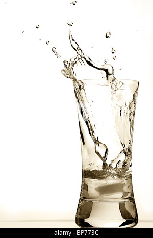 an ice cube is thrown into a glass of water, water splashes fly from a ...