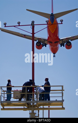 People working on runway approach lights beneath jet airplane landing at Los Angeles Int'l Airport LAX, California  Stock Photo