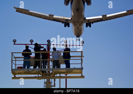 People working on runway approach lights beneath jet airplane landing at Los Angeles Int'l Airport LAX, California Stock Photo