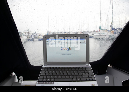 using netbook and 3g mobile internet access looking out of a boat canopy in the rain in a marina in the uk Stock Photo
