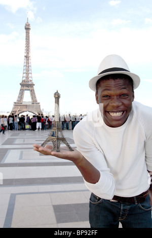 Young Man holding a mini Eiffel tower souvenir in front of the eiffel tower. Stock Photo