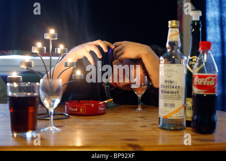Drunk man sitting at a table with alcohol bottles, Berlin, Germany Stock Photo