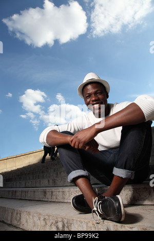 Young black man smiling and sitting on steps on a sunny day in Paris, France near Trocadero. Stock Photo
