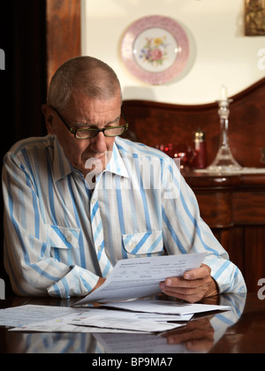 Elderly man sitting at a desk looking through bills Stock Photo