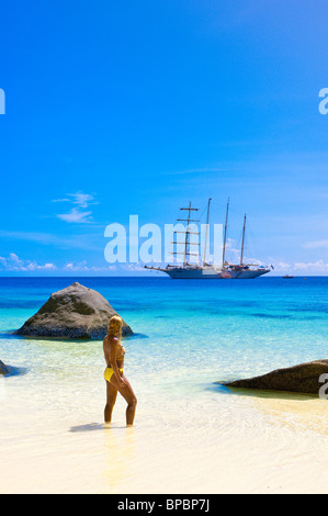 Woman in bikini on beach with star flyer clipper ship anchored off Ko Miang Island Similan Islands in the Andaman Sea, Thailand. Stock Photo