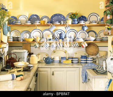 Collection of blue+white striped Cornish-ware crockery on shelves in pale yellow cottage kitchen