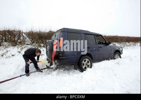 Man digging out snowed in four-wheel drive, Dartmoor, Devon Stock Photo