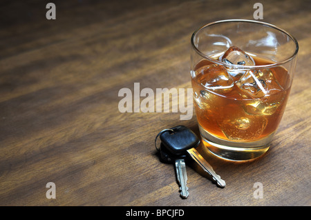 Glass of whiskey and car keys on wooden table.