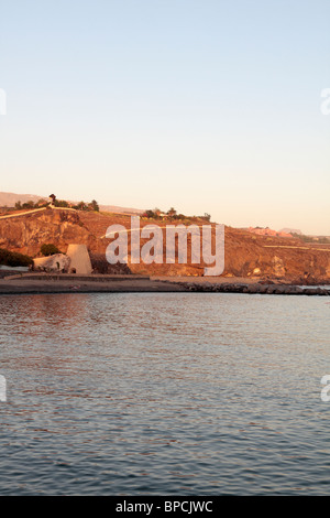 The cliffs and lime kiln at the end of Playa San Juan with the Abama resort on the horizon and clear blue sky and calm sea Tener Stock Photo