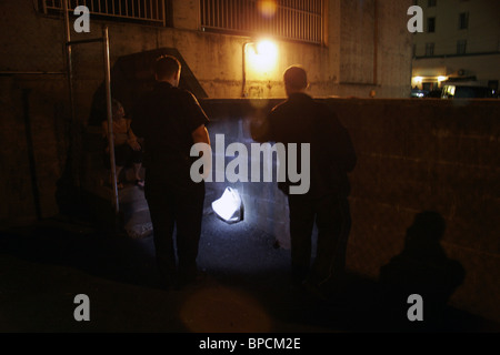 A police officer approaches a couple in an alley known to be used for vice in the Downtown Eastside, Vancouver, Canada Stock Photo