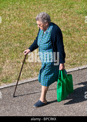 Older woman with shopping bag and stick walking along pavement - France. Stock Photo
