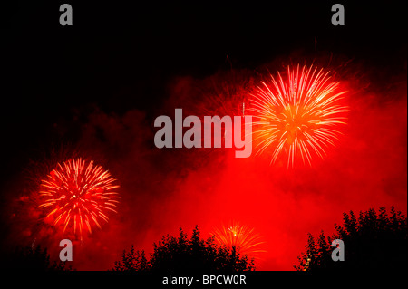 Firework bursts in the night sky against a background of red smoke. Space for text in the dark of the night sky. Stock Photo
