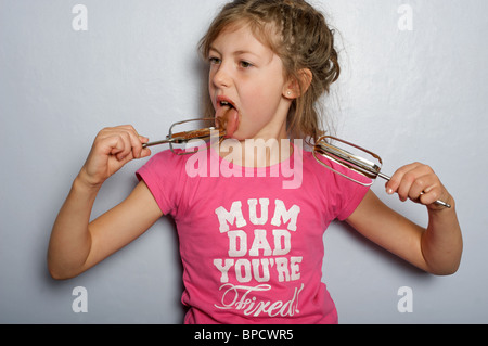 Young girl licking chocolate icing from the whisks of a blender Stock Photo