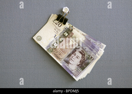 £20 notes hanging from a bulldog clip against a blue cloth background Stock Photo