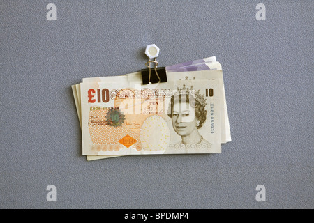 Sterling £20 and £10 notes hanging from a bulldog clip against a blue cloth background Stock Photo