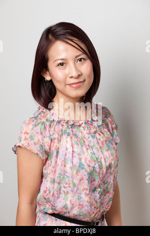 Portrait of a Smiling Young Asian Woman in a Floral Blouse Against a Neutral Background. Stock Photo