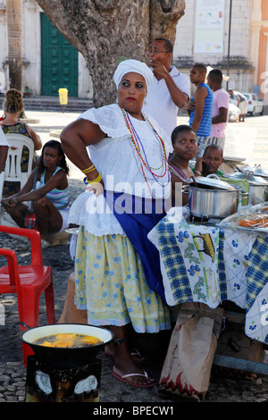 Bahian woman in traditional white dress (Baiana) selling street food at the Pelourinho district, Salvador, Bahia, Brazil. Stock Photo