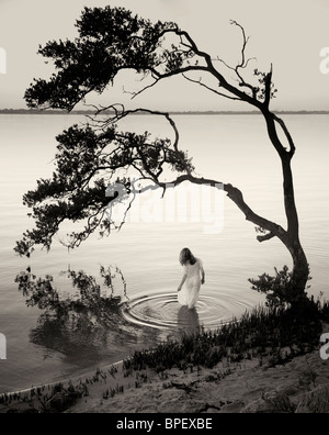 Black and white of woman standing in water under a tree Stock Photo