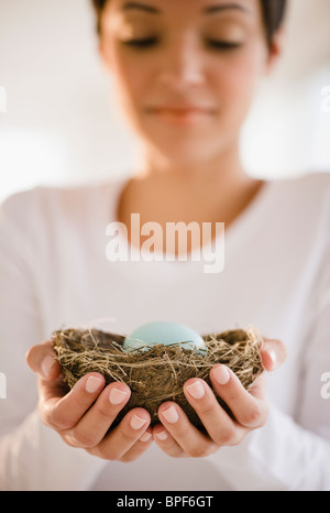 Mixed race woman holding nest with egg Stock Photo