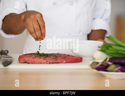 Mixed race chef seasoning steak Stock Photo