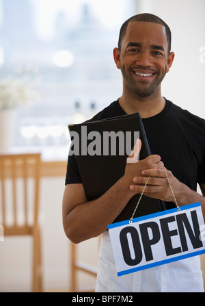 Mixed race waiter in restaurant holding menu and open sign Stock Photo