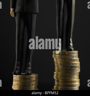 Two Figures In Black Suits Standing On Top Of Two Piles Of Pound Sterling Coins Stock Photo