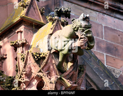 Gargoyle in the form of a seated man holding his nose, on Freiburg Münster, Freiburg im Breisgau, Baden Wurtemburg, Germany Stock Photo