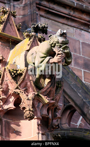 Gargoyle in the form of a seated man holding his nose and vomiting, on Freiburg Münster, Freiburg im Breisgau, Germany Stock Photo