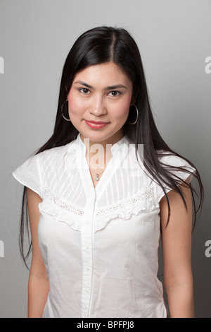Portrait of a young woman with long dark hair wearing a white blouse and hoop earrings, looking at the camera with a gentle smile. Stock Photo