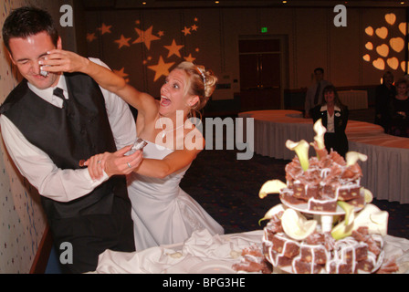 beautiful newly weds cutting wedding cake bride putting cake in grooms face Stock Photo