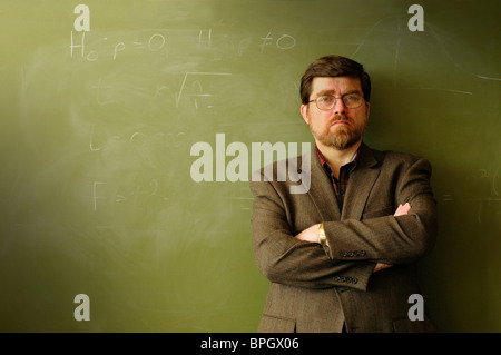 Math professor or teacher standing in front of a green chalkboard, possibly annoyed or determined. Stock Photo
