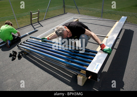 Man assembling solar panels on roof. Vacuum tubes to heat water. Stock Photo