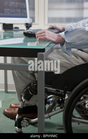 Man in a wheelchair working at desk in a home office Stock Photo