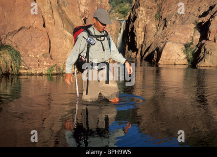 Man hiking through the river with water fall in background. Stock Photo