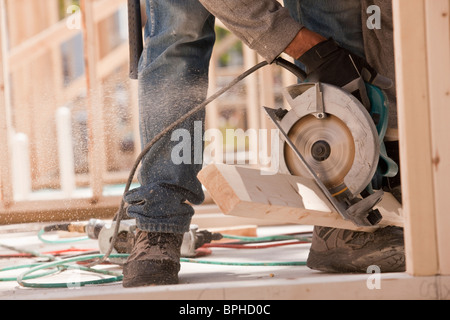 Carpenter sawing a plank at a construction site Stock Photo