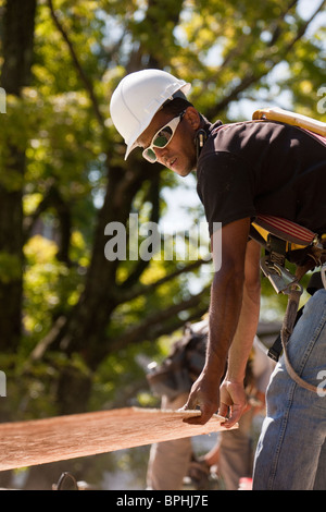 Carpenter carrying a particle board at a construction site Stock Photo