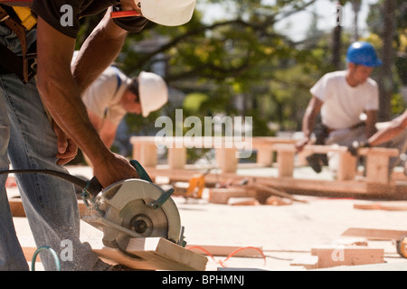 Carpenters using circular saw at a construction site with gable frame in the background Stock Photo