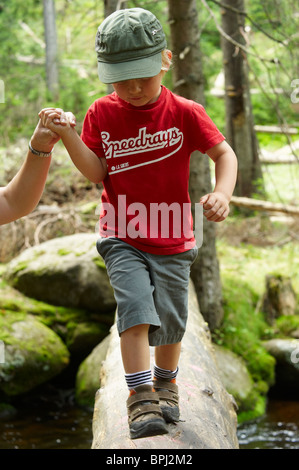 Children exploring in forest - mother helping son over stream - National Park Sumava Czech Republic Stock Photo