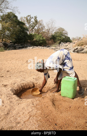 A blind woman collects water from a dry river bed in northern Ghana, West Africa Stock Photo